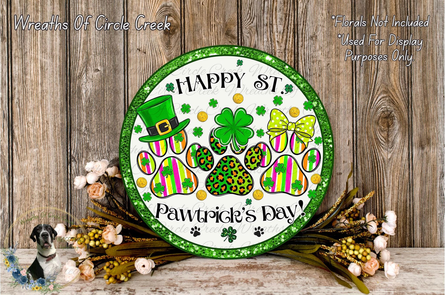 A circular sign with a green border and the text "Happy St. Pawtitive's Day!" surrounded by paw prints, a leprechaun, and various other festive elements. The sign is displayed on a wooden surface, with a floral arrangement and a small dog in the background.