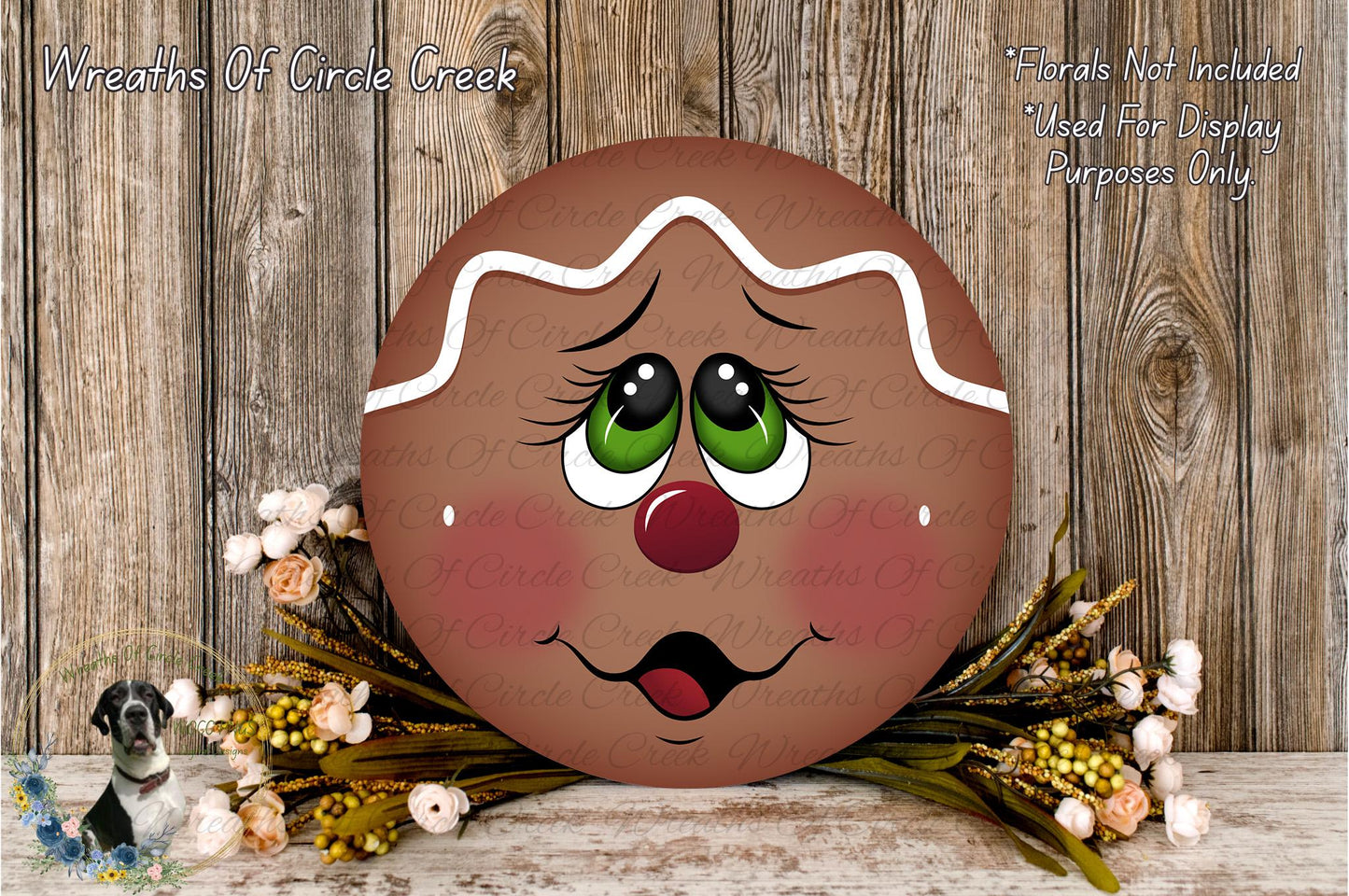 A gingerbread man-themed wreath with a face and eyes, placed on a wooden surface surrounded by flowers.