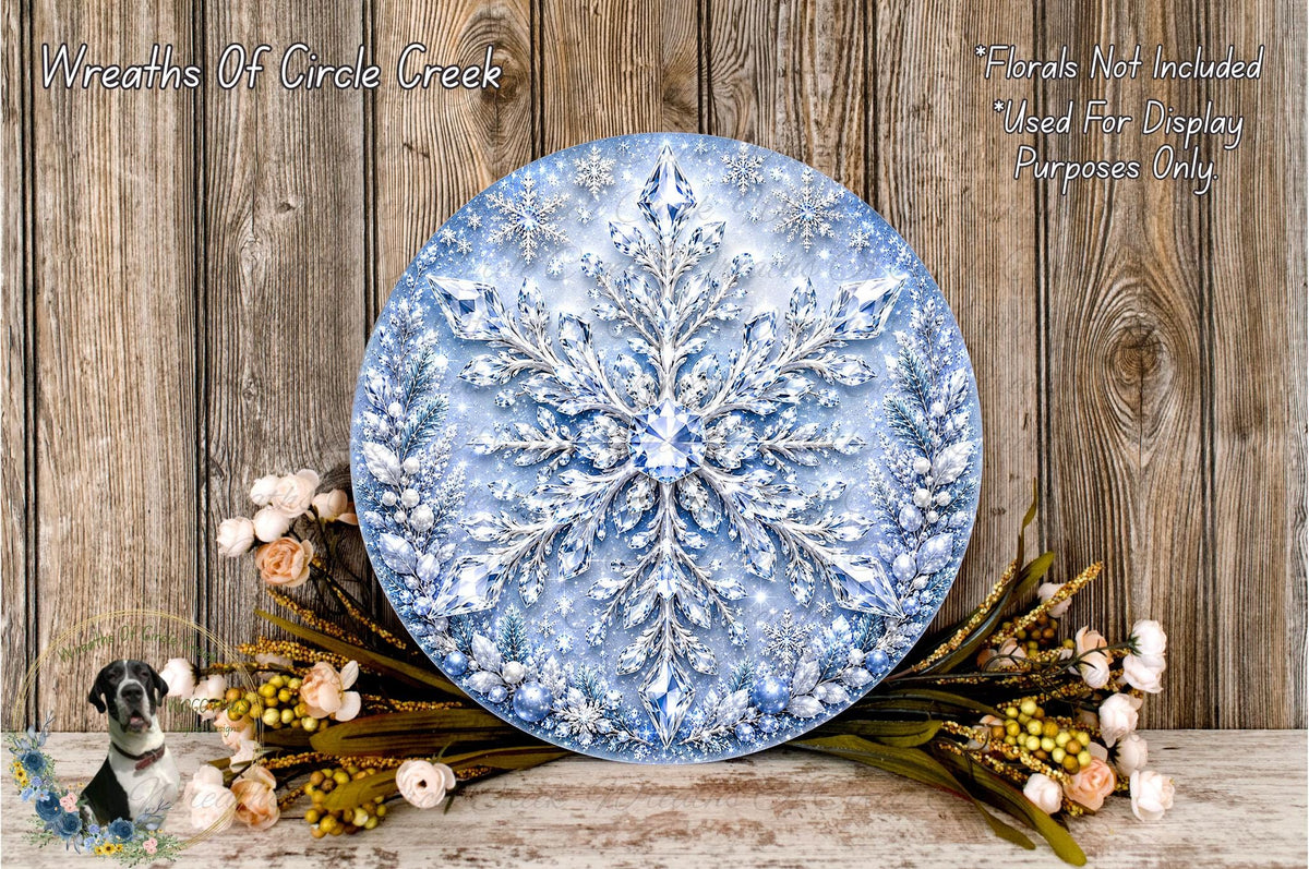 A large, round wreath made of blue and white materials, resembling a snowflake, is displayed on a wooden surface. The wreath is surrounded by a variety of flowers and greenery, creating a festive and natural setting.