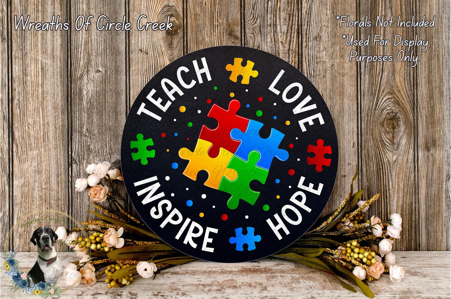 A black sign with colorful puzzle pieces and the words "Teach Love Inspire Hope" written on it, surrounded by flowers and greenery.