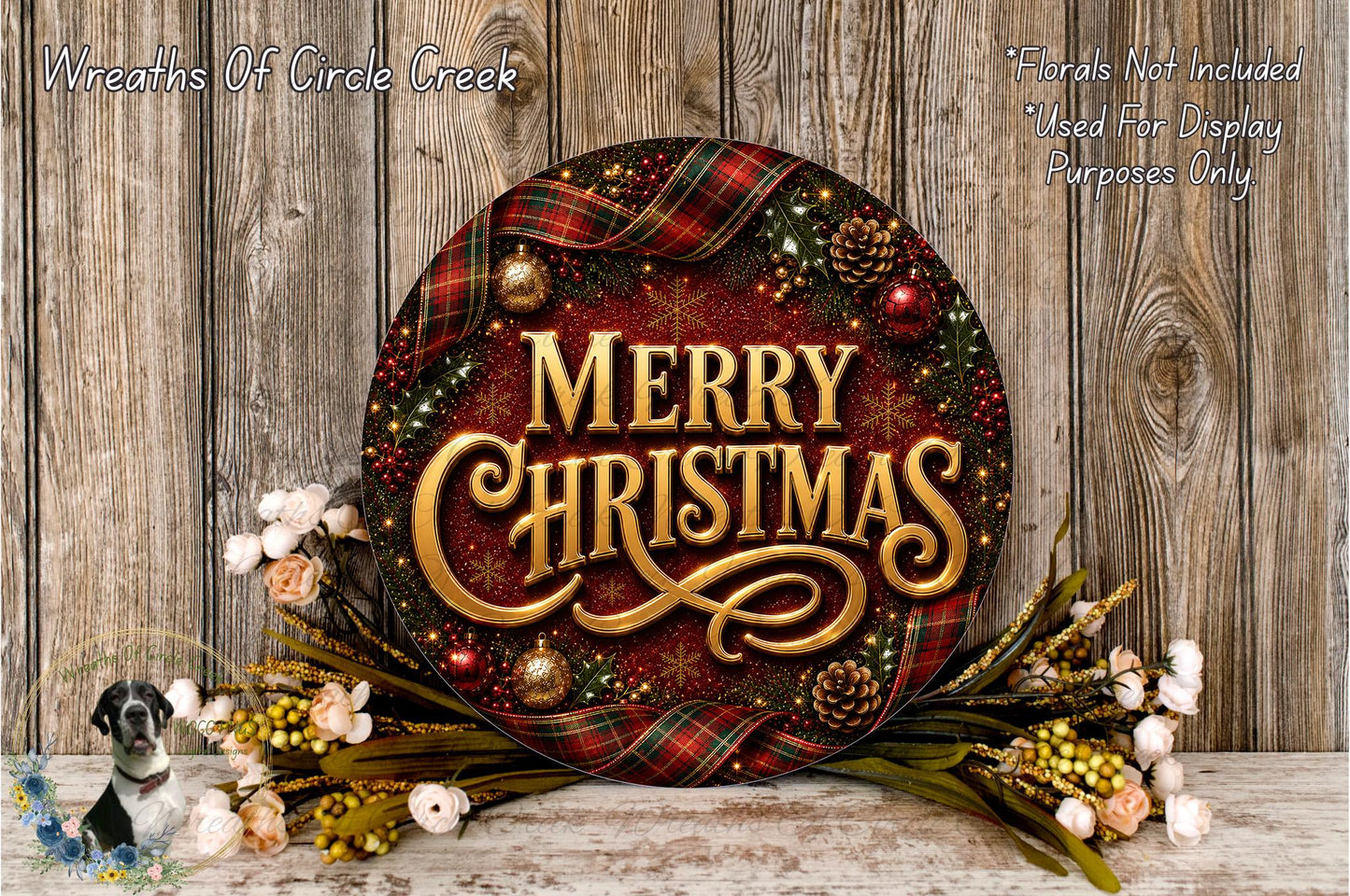 A festive Christmas wreath with the text "Merry Christmas" displayed prominently. The wreath is adorned with various holiday decorations, including pine cones, ornaments, and a plaid ribbon. The wreath is placed on a wooden surface, and there are also some flowers and greenery surrounding it.