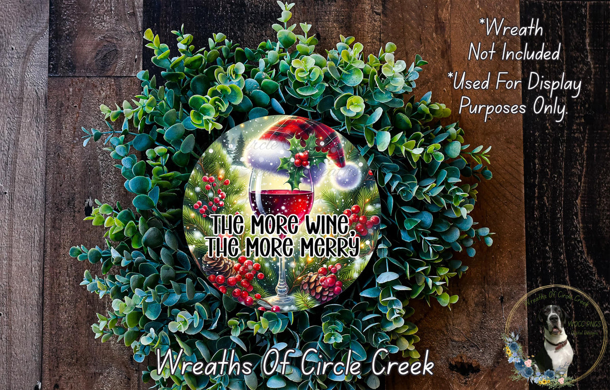 a wreath made of green leaves and red berries, with a wine glass and a red and white plaid hat on top. The wreath is displayed on a wooden surface, and there is a text overlay that reads "The more wine, the merrier" and "Wreaths of Circle Creek".