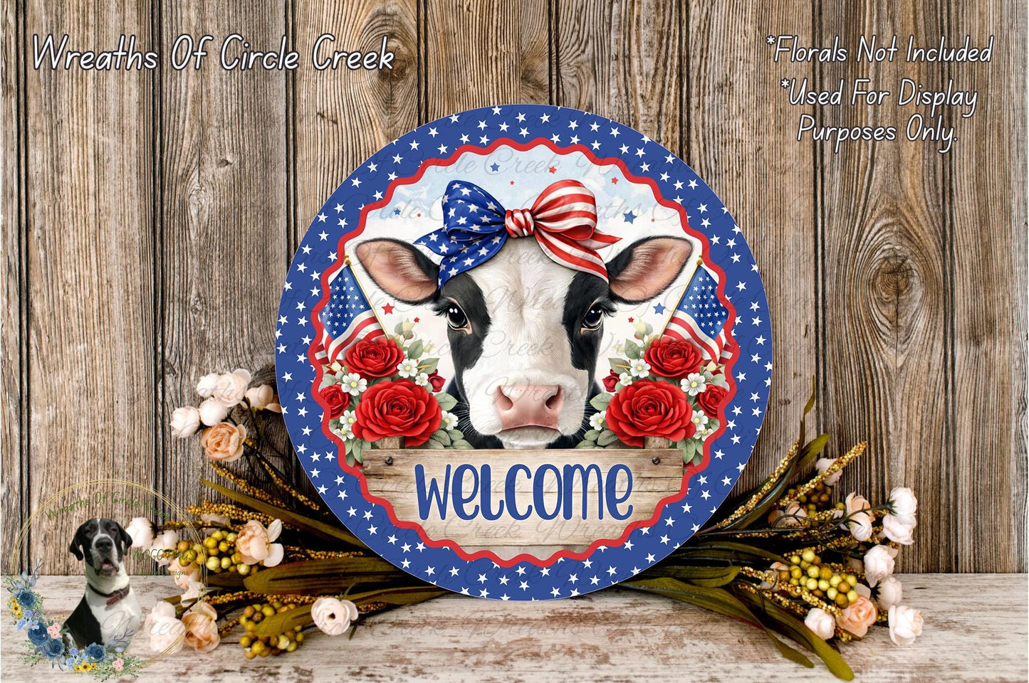 a decorative sign with a cow's face, surrounded by flowers and a bow, placed on a wooden surface.