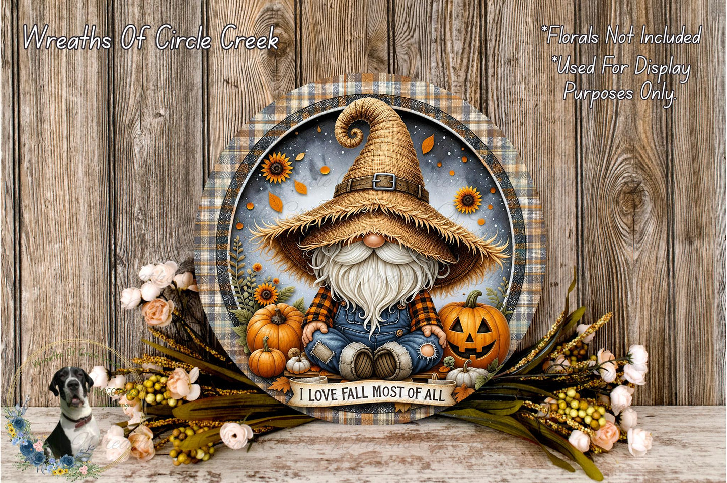A gnome wearing a straw hat and holding a pumpkin is surrounded by autumn-themed decorations, including flowers and pumpkins, on a wooden surface.