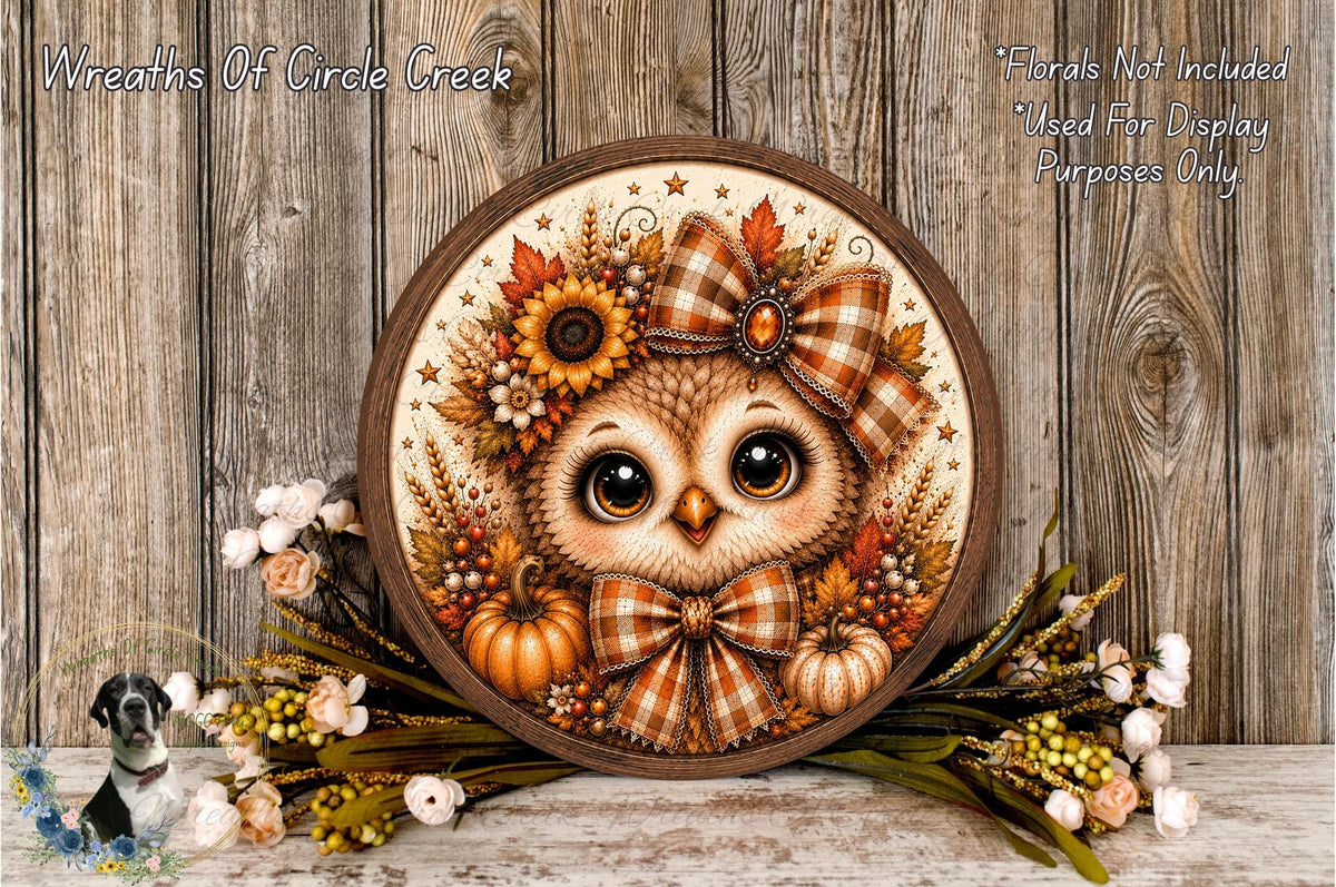 a decorative wreath with an owl design, surrounded by autumn foliage and flowers, placed on a wooden surface.