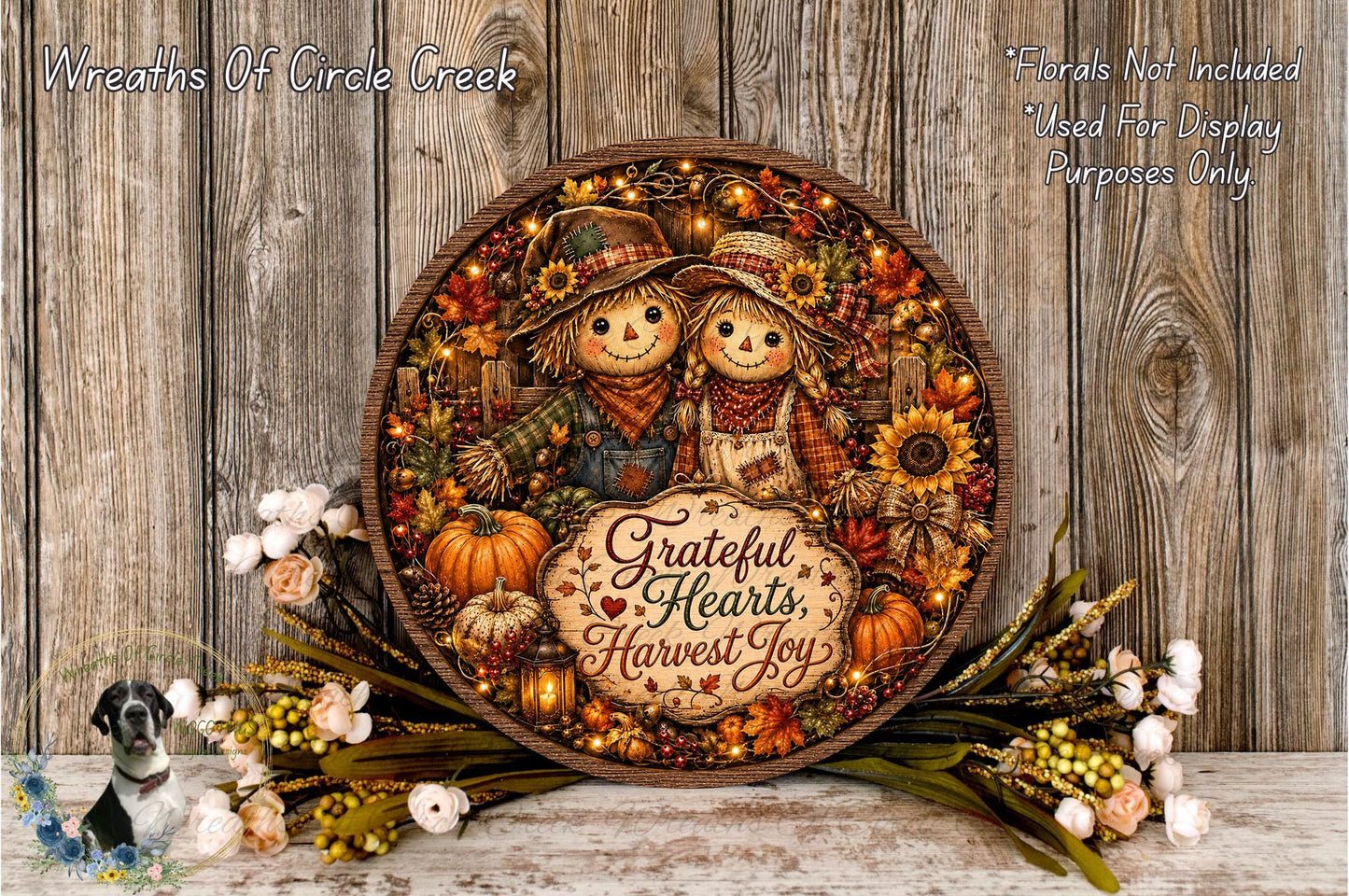 A decorative wreath with a couple of scarecrow figures, surrounded by autumn-themed elements such as pumpkins, sunflowers, and pine cones. The wreath is placed on a wooden surface, and there are flowers and greenery surrounding it.