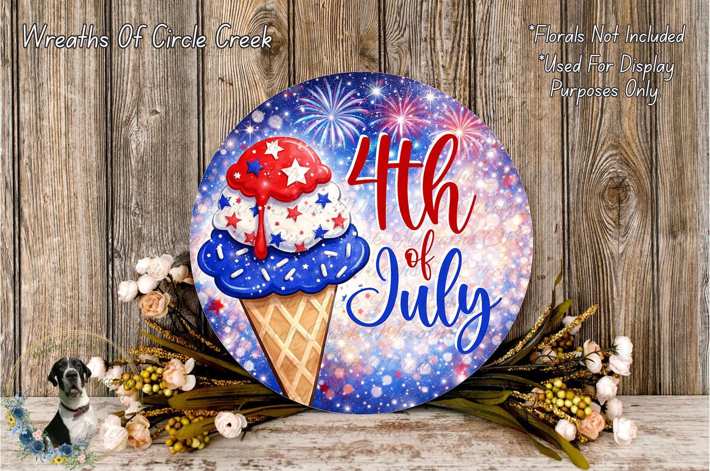 A circular sign with a patriotic design, featuring a red, white, and blue ice cream cone with fireworks in the background, surrounded by flowers and placed on a wooden surface.