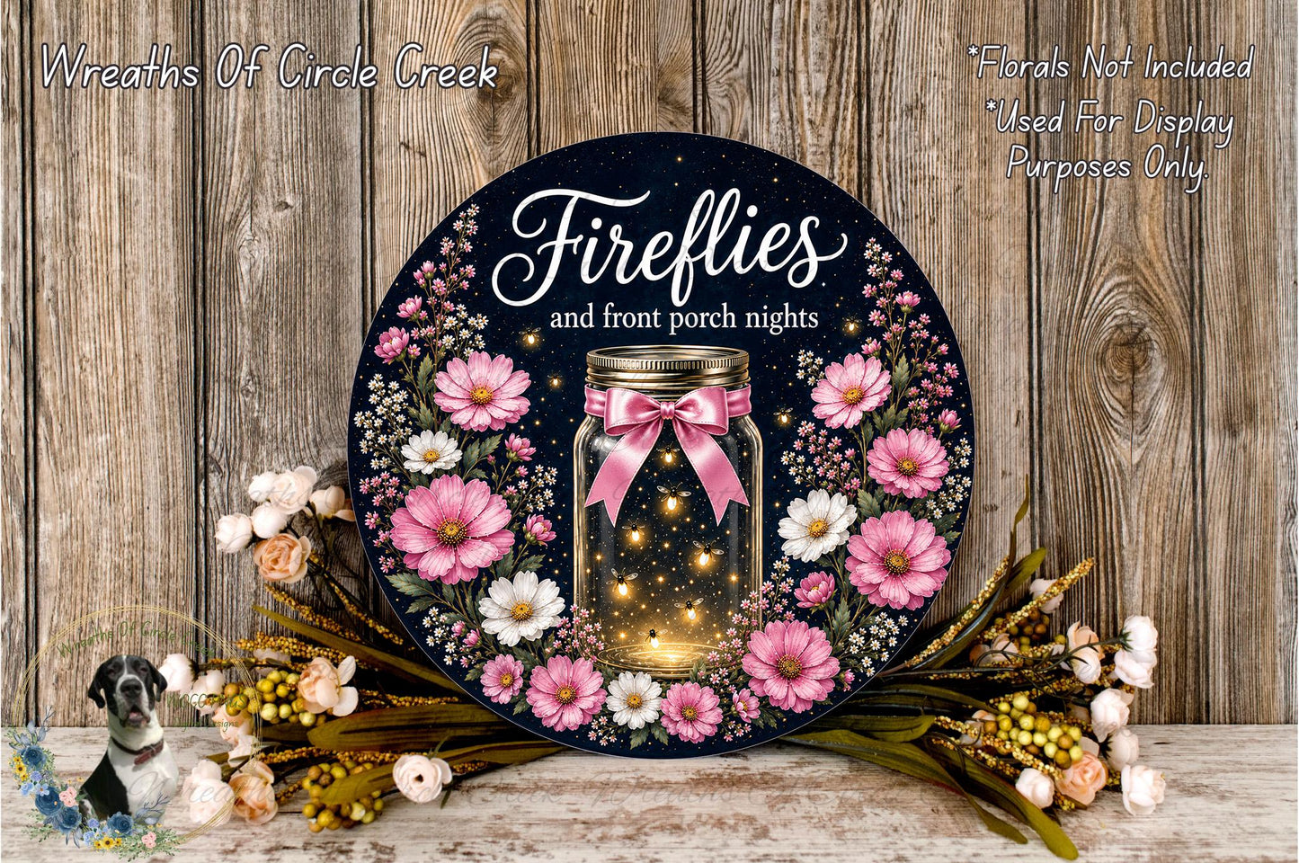 a decorative wreath with a jar of fireflies, surrounded by pink and white flowers, placed on a wooden surface.
