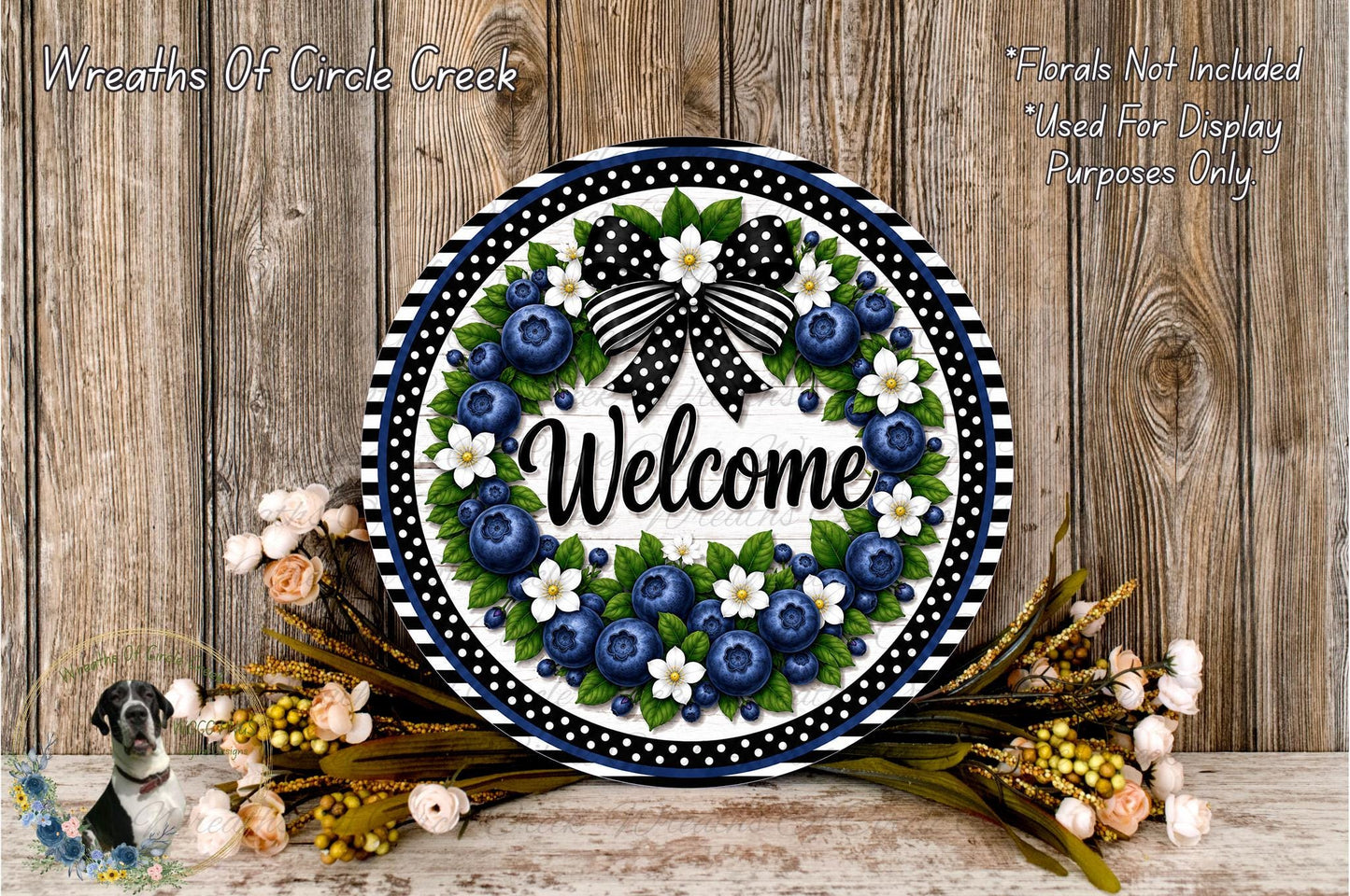 A decorative wreath with the word "Welcome" on it, surrounded by various flowers and foliage, placed on a wooden surface.