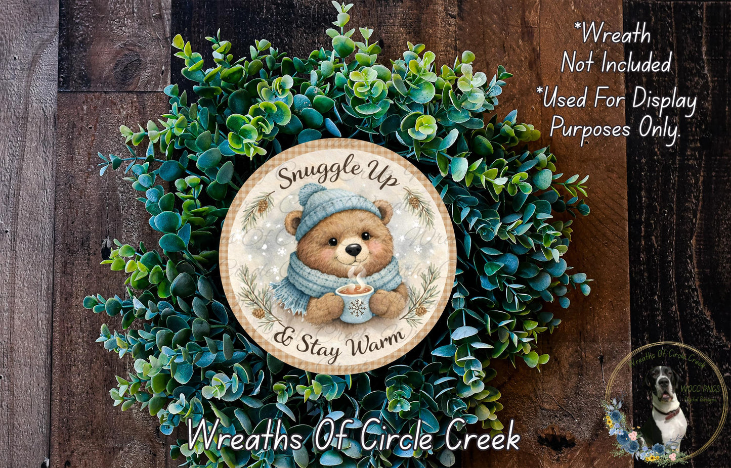 A wreath made of green leaves and a brown teddy bear wearing a blue scarf, with the text "Snuggle up & stay warm" and "Wreaths of Circle Creek" displayed on it.