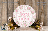 a round sign with a floral design and the text "bless this home" displayed on it, surrounded by a bouquet of flowers and greenery.