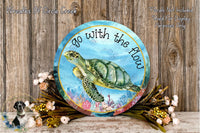 a round sign with a turtle on it, surrounded by flowers and placed on a wooden surface.