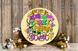 a decorative sign with a colorful and whimsical design, surrounded by flowers and placed on a wooden surface.