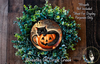 A Halloween-themed wreath with a black cat sitting in a carved pumpkin, surrounded by greenery.
