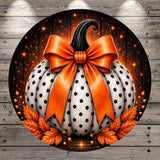A large, white pumpkin with black polka dots and an orange ribbon bow is displayed against a dark background with orange and white lights.