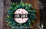 a wreath made of green leaves and a white circular sign with the text "LOVE SHACK" in red and black letters.