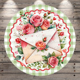 A decorative round plate with a floral design featuring pink roses and green leaves surrounding a white envelope.