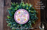 a wreath made of green leaves and flowers, with a purple and white sign that reads "Home Sweet Home" in the center. The sign is surrounded by the wreath, creating a decorative and festive display.