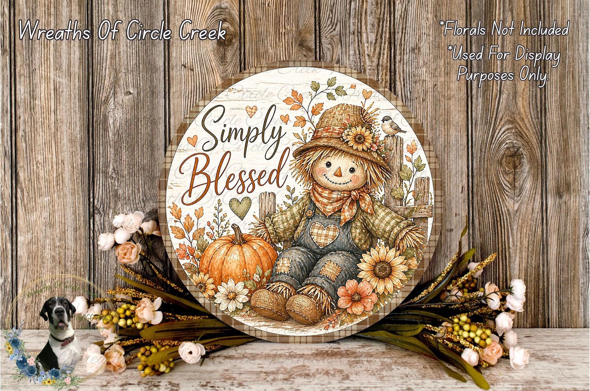 A round wooden sign with a scarecrow and autumn decorations, including a pumpkin and flowers, is displayed against a wooden background.