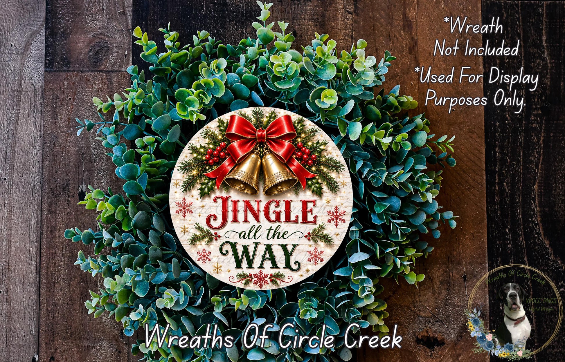a Christmas wreath with a decorative sign that says "Jingle all the Way". The wreath is made of green leaves and has a red ribbon and bells attached to it. The sign is placed in the center of the wreath. The background of the image is a wooden surface with a dog visible in the bottom right corner.