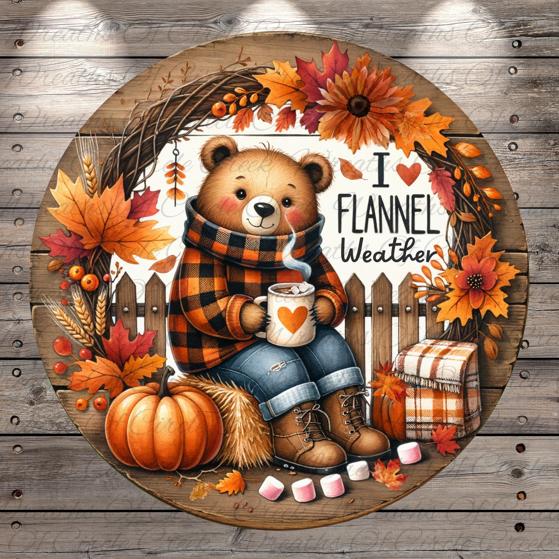 A round wooden sign featuring a teddy bear wearing a plaid sweater and holding a cup of hot chocolate, surrounded by autumn decorations such as a wreath, pumpkins, and leaves.