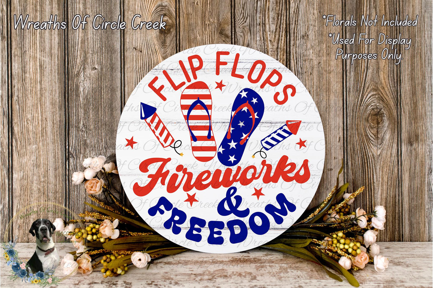 A circular sign with the text "FLIP FLOPS FIREWORKS & FREEDOM" surrounded by fireworks and flip flops, placed on a wooden surface with flowers.