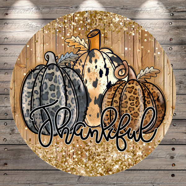 A circular graphic with a wooden background and three leopard print pumpkins. The pumpkins are decorated with leaves and the word "Thankful" written in cursive text.