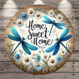 A circular wooden sign with a floral design and two blue dragonflies. The sign has the text "Home Sweet Home" written on it.