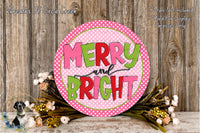 A circular sign with the text "MERRY AND BRIGHT" in pink and green colors, surrounded by a floral arrangement and placed on a wooden surface.