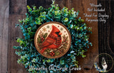 A wreath made of green foliage and a red cardinal bird, with a circular design featuring a bird and snowflakes.