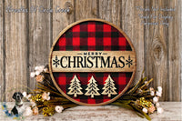 A round wooden sign with a red and black plaid pattern, displaying the text "Merry Christmas" in bold letters. The sign is surrounded by a wreath of flowers and greenery, creating a festive holiday display.