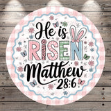 A circular design with a pink and white checkered border, featuring the text &quot;He is Risen Matthew 28:6&quot; surrounded by various Easter-themed elements such as flowers, butterflies, and Easter eggs.
