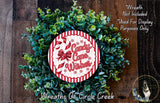 a wreath made of green leaves and a red and white circular sign with the text "Candy cane wishes" on it. The sign is surrounded by a wreath made of similar green leaves. The background is a wooden surface with a dog visible in the bottom right corner.