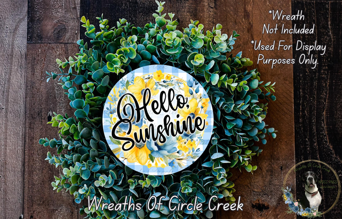 a wreath made of various green plants and flowers, with a blue and yellow circular sign that says "Hello. Sunshine" in the center.