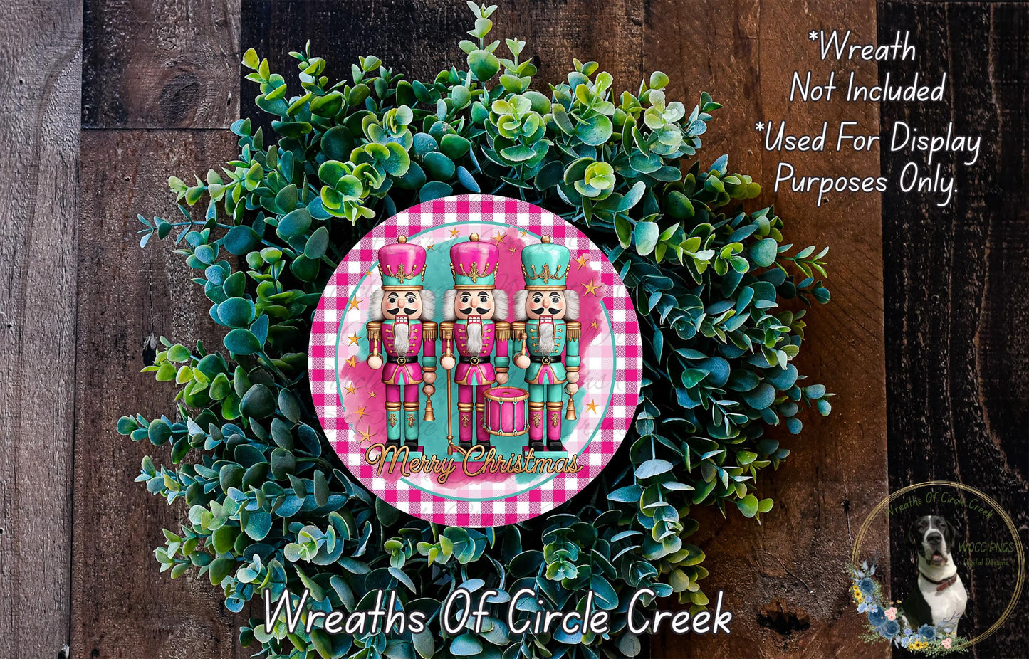 A wreath made of green foliage and featuring three nutcracker characters in a pink and green color scheme, with the text "Merry Christmas" displayed on the wreath.