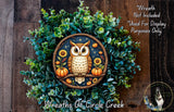 A wreath featuring an owl surrounded by autumnal elements such as pumpkins, sunflowers, and pine cones, set against a backdrop of greenery.