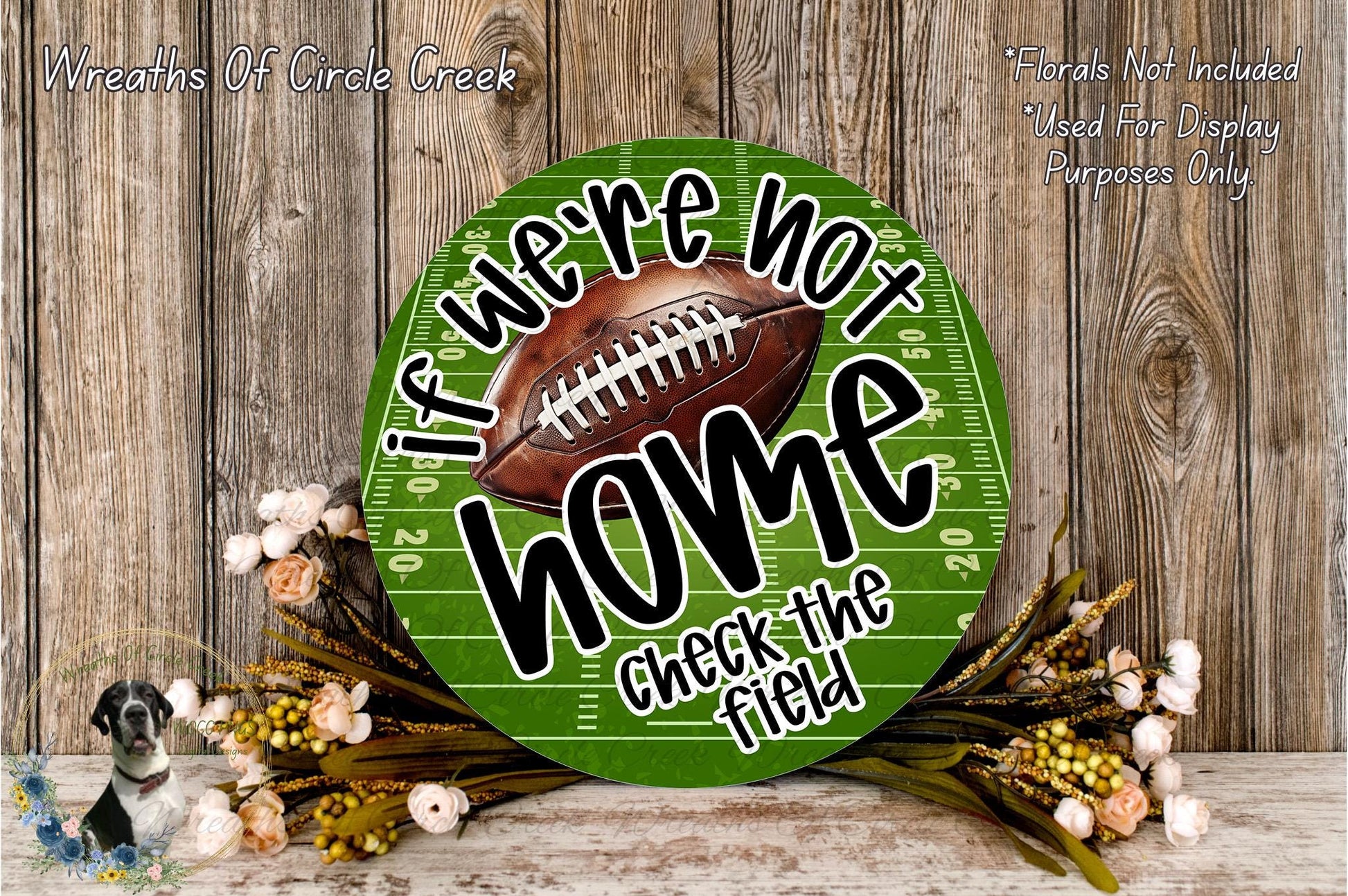 a green football field sign with the text "If we're not home, check the field" displayed on it. The sign is surrounded by a floral arrangement and a wooden background.