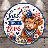 A circular design featuring a Highland cow wearing an American flag-themed bow tie, surrounded by flowers and fireworks. The text "Land that I Love" is displayed on the design.