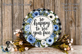 a decorative wreath with a floral design and the text "So happy to see your face" written on it. The wreath is surrounded by various flowers, including blue and white flowers, and is placed on a wooden surface.