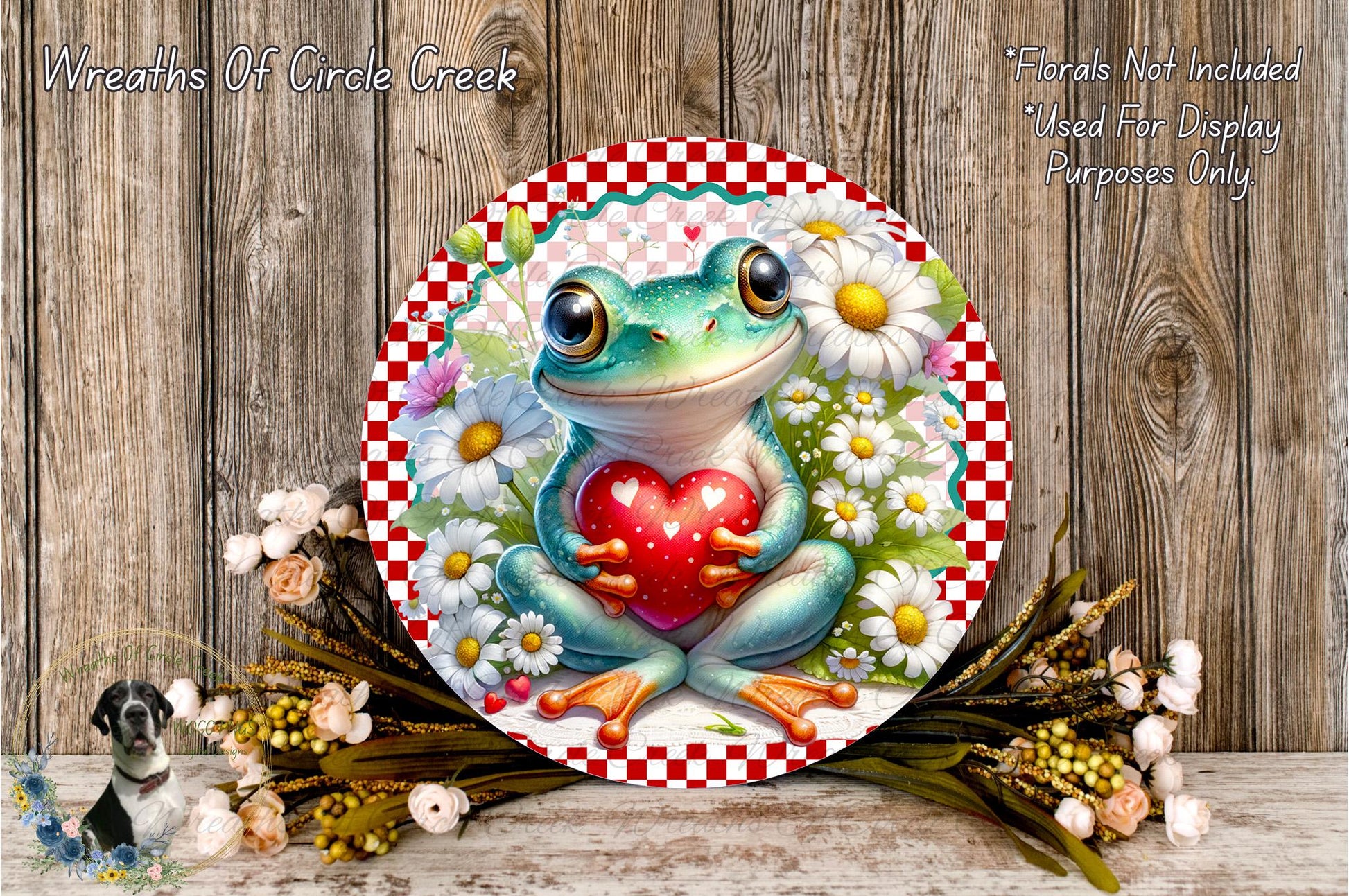A round, decorative plate featuring a green frog holding a red heart, surrounded by a floral arrangement and placed on a wooden surface.