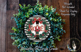 A wreath made of green leaves and a nutcracker figure, with the word "Noel" displayed on it. The wreath is placed on a wooden surface.