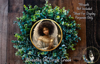 a wreath with a portrait of a woman, surrounded by green foliage. The wreath is displayed on a wooden background, and there is a small dog in the bottom right corner of the image.