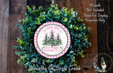 a wreath made of green foliage and a circular sign with a Christmas tree design, placed on a wooden surface.