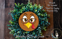 A wreath made of green plants and a cartoon turkey face with glasses, with text indicating that the wreath is not included in a display and is used for purposes only.