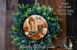 A wreath made of green leaves and autumn-themed decorations, including a girl holding a coffee mug and a sign that says "Welcome".