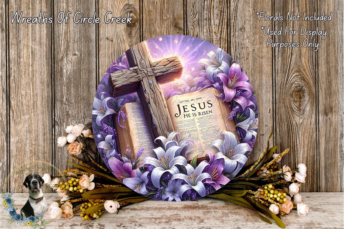 A wreath with a cross and a book of the Bible, surrounded by purple and white flowers, placed on a wooden surface.