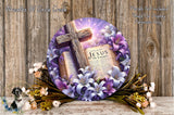 A wreath with a cross and a book of the Bible, surrounded by purple and white flowers, placed on a wooden surface.