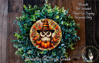 A wreath made of green leaves and orange pumpkins, featuring an owl wearing a witch's hat and surrounded by pumpkins.