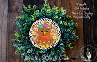 A wreath made of green plants and featuring a colorful illustration of a brown bird with a bow on its head.