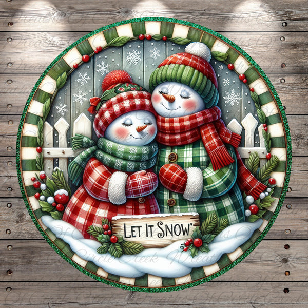 A festive winter scene featuring two cheerful snowmen, one wearing a green and red plaid outfit and the other in a red and green plaid outfit, standing together and smiling. The snowmen are surrounded by a wreath of berries and a sign that reads "Let it snow". The background includes a snowy landscape with a fence and trees covered in snow.